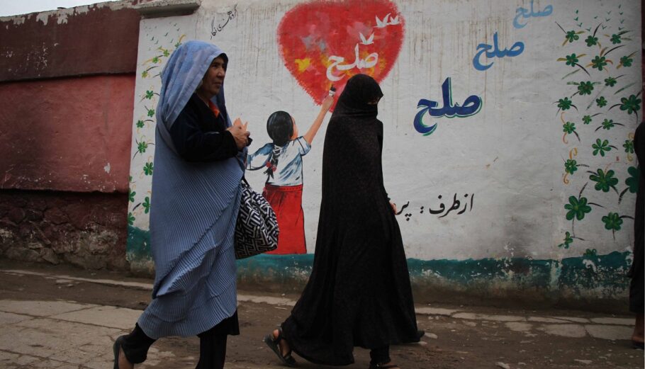 Αφγανές γυναίκες περνούν από έναν τοίχο με γκράφιτι που γράφει «Ειρήνη» στη Χεράτ ©EPA/JALIL REZYEE