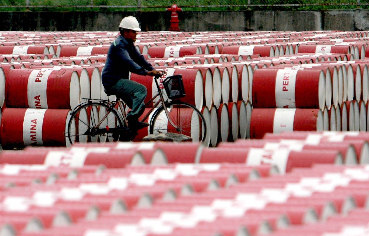 Eργάτης σε ποδήλατο ανάμεσα σε βαρέλια πετρελαίου © EPA/BAGUS INDAHONO